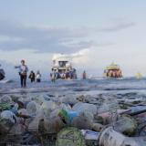 Tourists and local residents disembark from a boat onto a trash-polluted shore, in Sanur, Denpasar, Bali, Indonesia
