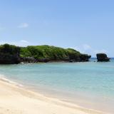 A golden sandy shoreline with light crystal blue waters is captured in Okinawa, Japan