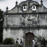 The front facade of a colonial church is pictured against the backdrop of a gray and cloudy sky