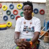 Jumoke Olowookere, a black woman wearing a white t-shirt, founder of the Waste Museum is photographed sitting on a painted tire