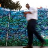 a priest, captured mid-step, is seen blurred against a crisp backdrop of repurposed, blue plastic bottles