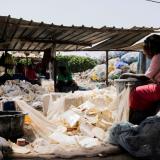 A woman sits with her back facing the camera as she washes plastic waste outside a landfill in Dakar, Senegal