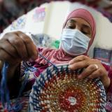 An Egyption woman wearing a pink headscarf a blue surgical mask is seen knitting a colorful bowl out of yarn made form recycled plastics