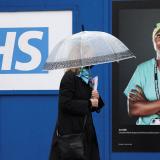 A woman walks past a poster of a NHS worker displayed on hoardings outside a temporary field hospital at St. George's Hospital, in London, Britain, on January 8, 2022