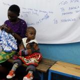 A mother sits on a wooden bench with her young daughter.