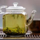 A glass tea kettle filled with tea and a brown tea cup sit on a wooden table. 