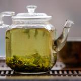 A glass tea kettle filled with tea and a brown tea cup sit on a wooden table. 