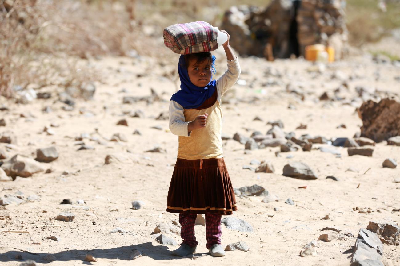 A displaced Yemeni girl carries a water gallon at a refugee camp.