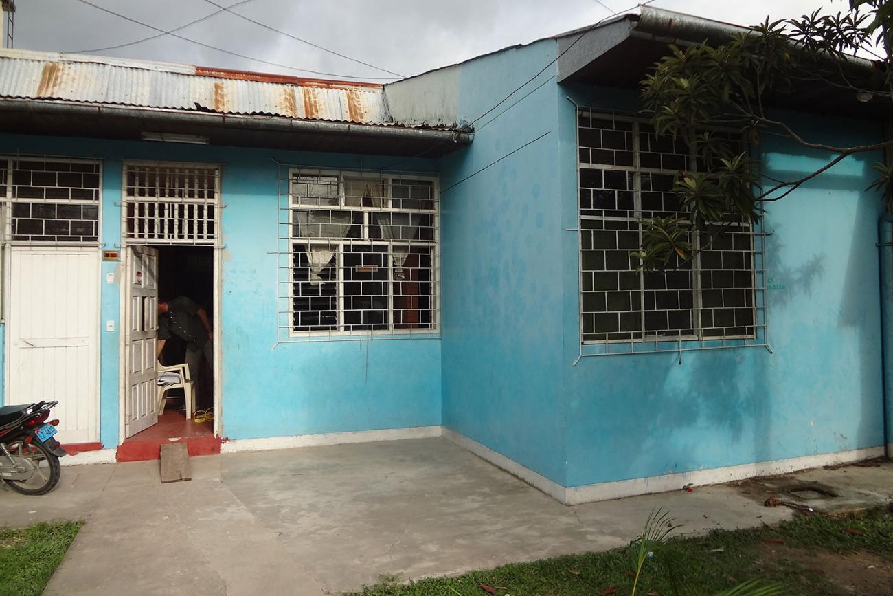 Picture shows a single-story, tin-roof home in town of Iquitos, Peru. The walls are blue, the skies are gray and there’s a lonely motorcycle parked in the yard.