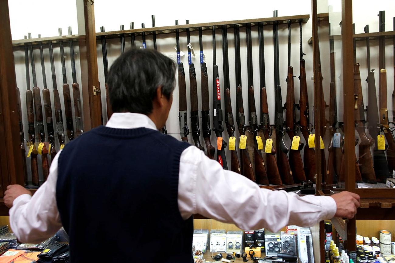 Picture shows a Japanese man standing with his back to the camera in a Tokyo gun shop on October 19, 2017, opening up a glass case filled with rifles lined up in a rack. They all have brightly colored price tags hanging from them.
