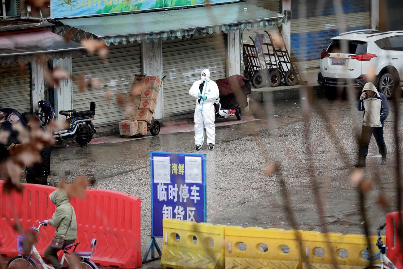 Picture shows the entrance to the market from a distance with a man wearing full protective gear stands out front. 