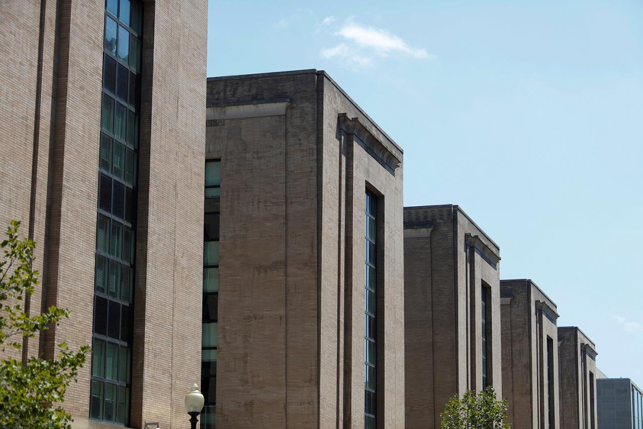 Picture shows a series of large, plain stone government buildings under a clear blue sky.