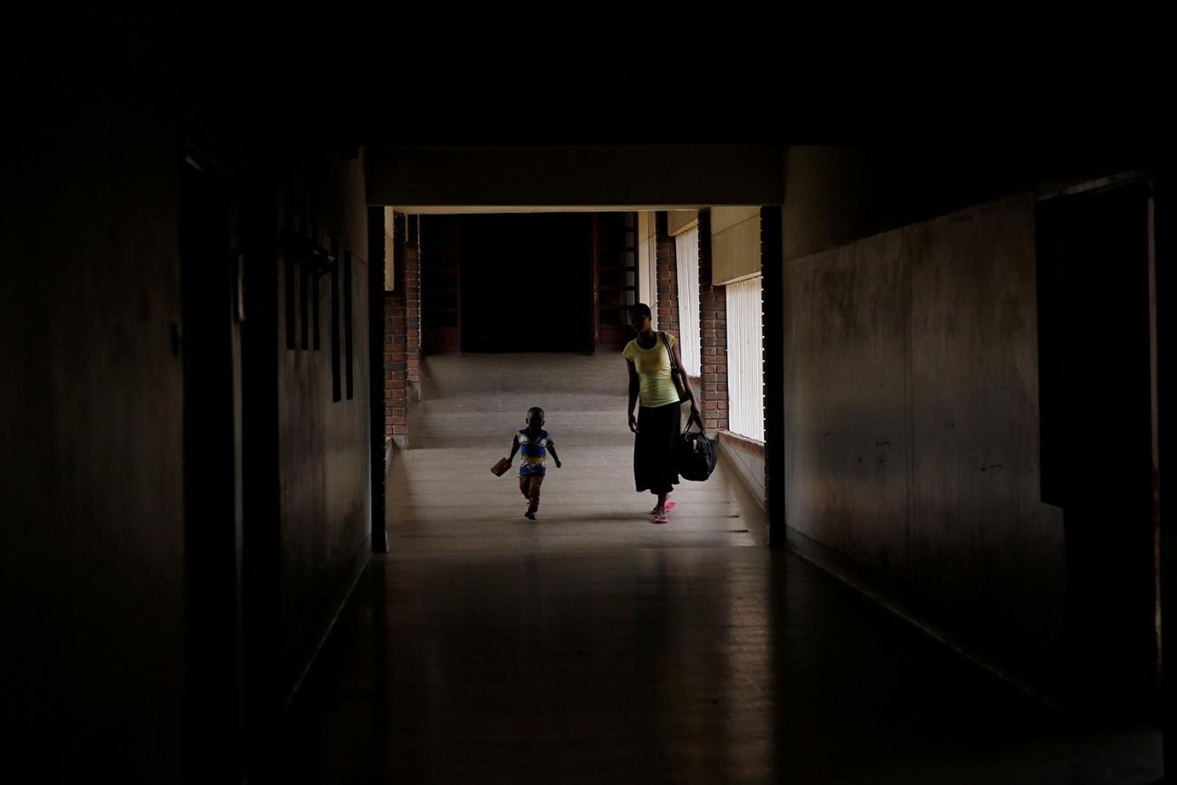 The photo shows a mother and child from a distance walking down a dark corridor in a dramatic photo. 