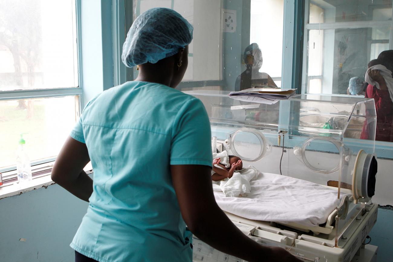 Picture taken from behind the nurse who is attending to a tiny baby. 