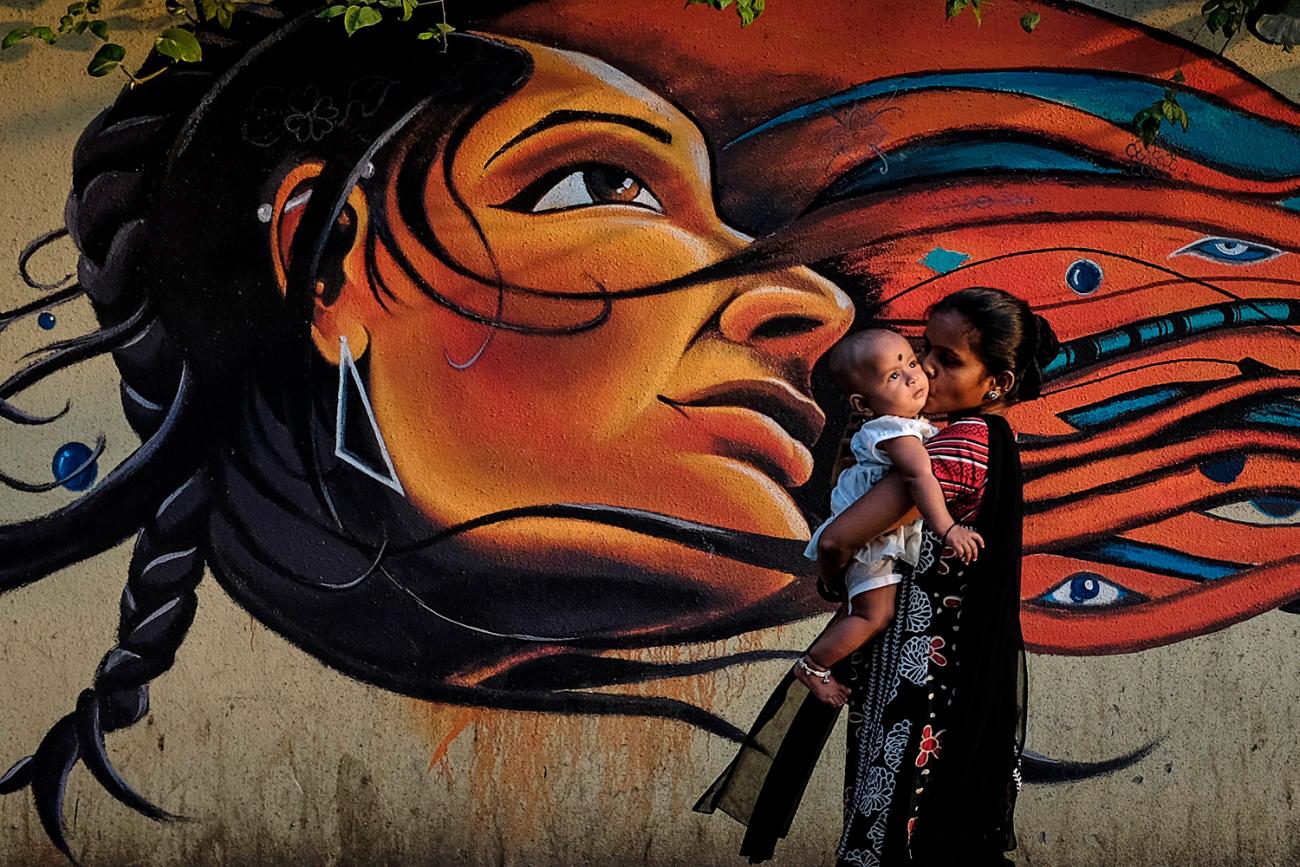 The image is striking with a large, artistic image behind a woman who is walking and holding a child.