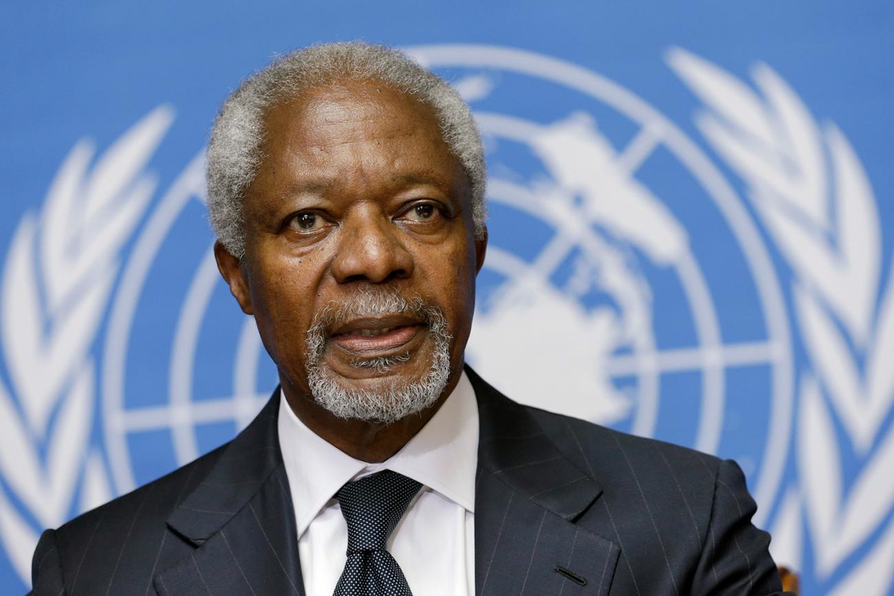 Photo shows a close-up head shot of Annan in front of a blue and white UN banner, which is blurred out in the background. 