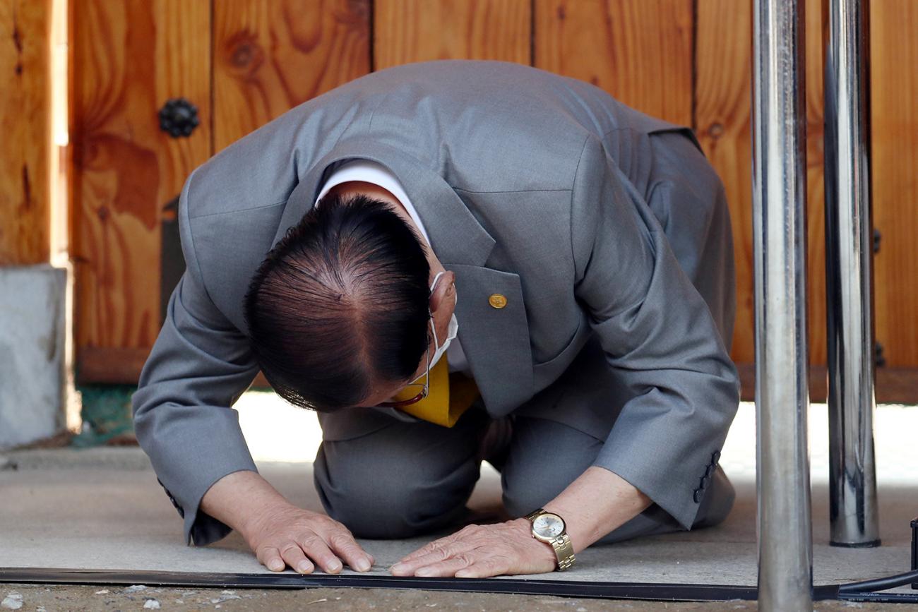 The image shows a well-groomed man in a nice suit on his hands and knees prostrate to the camera. 