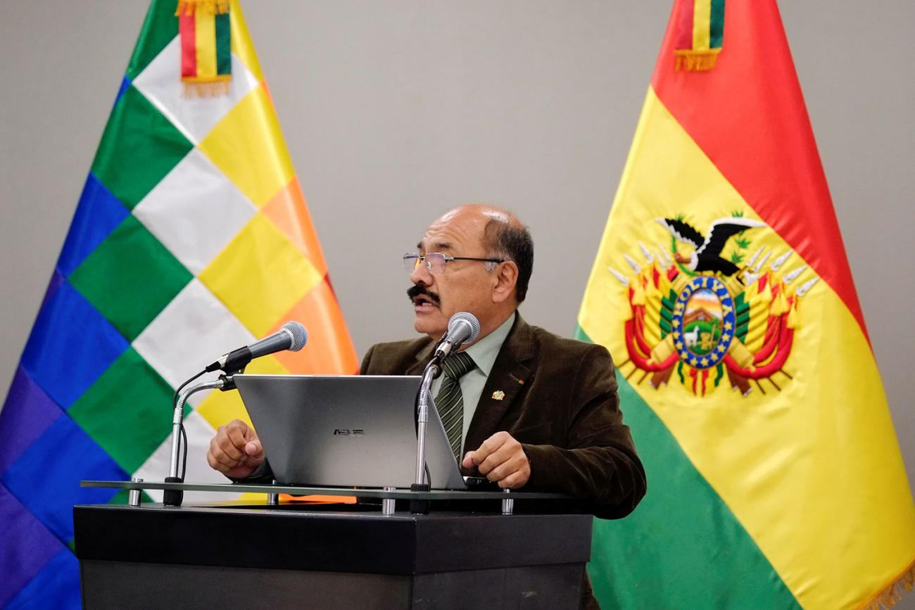 The photo shows the president standing behind a podium with country flags in the background. 