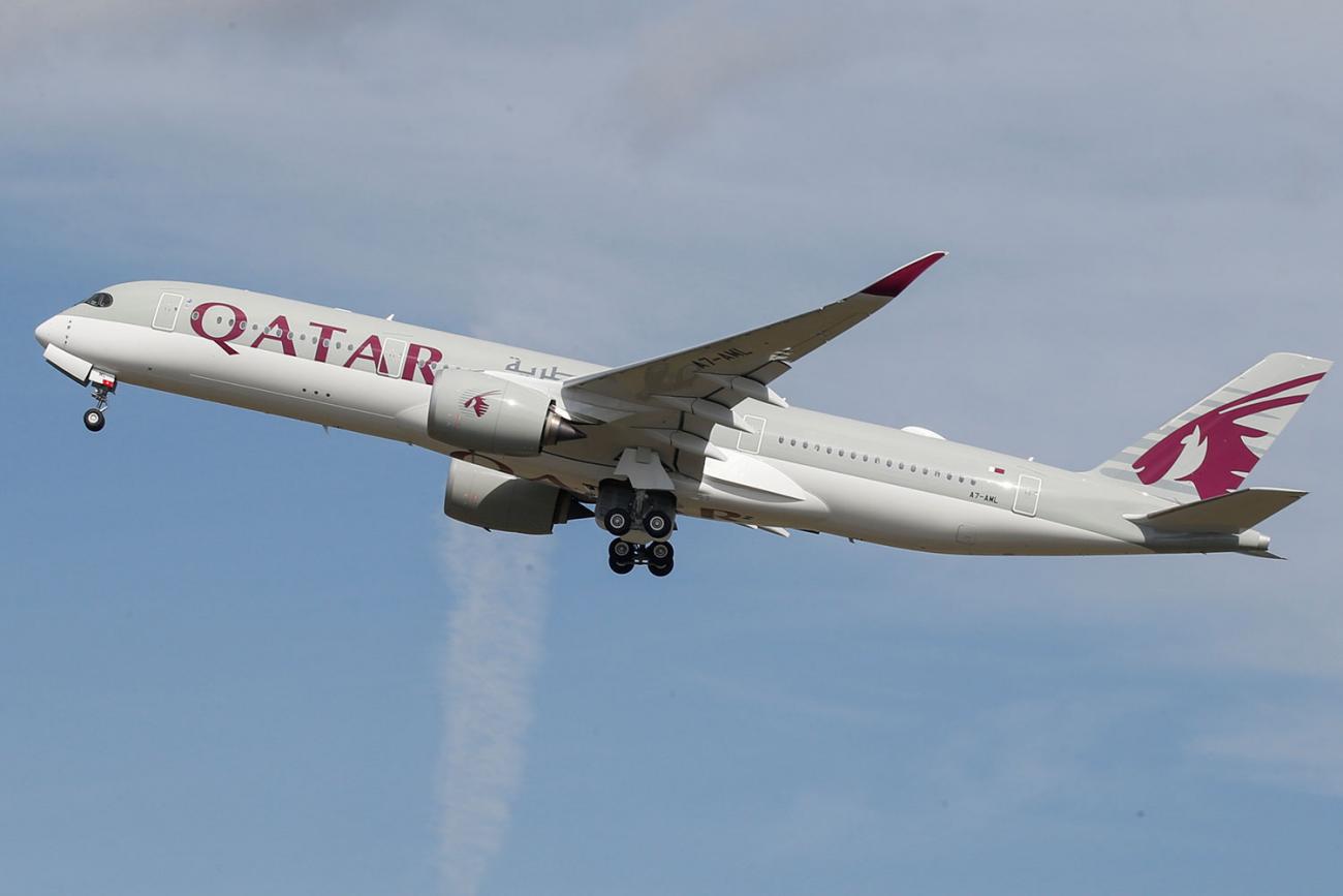 The photo shows a Qatar Airways jetliner in takeoff against a bright blue sky. 