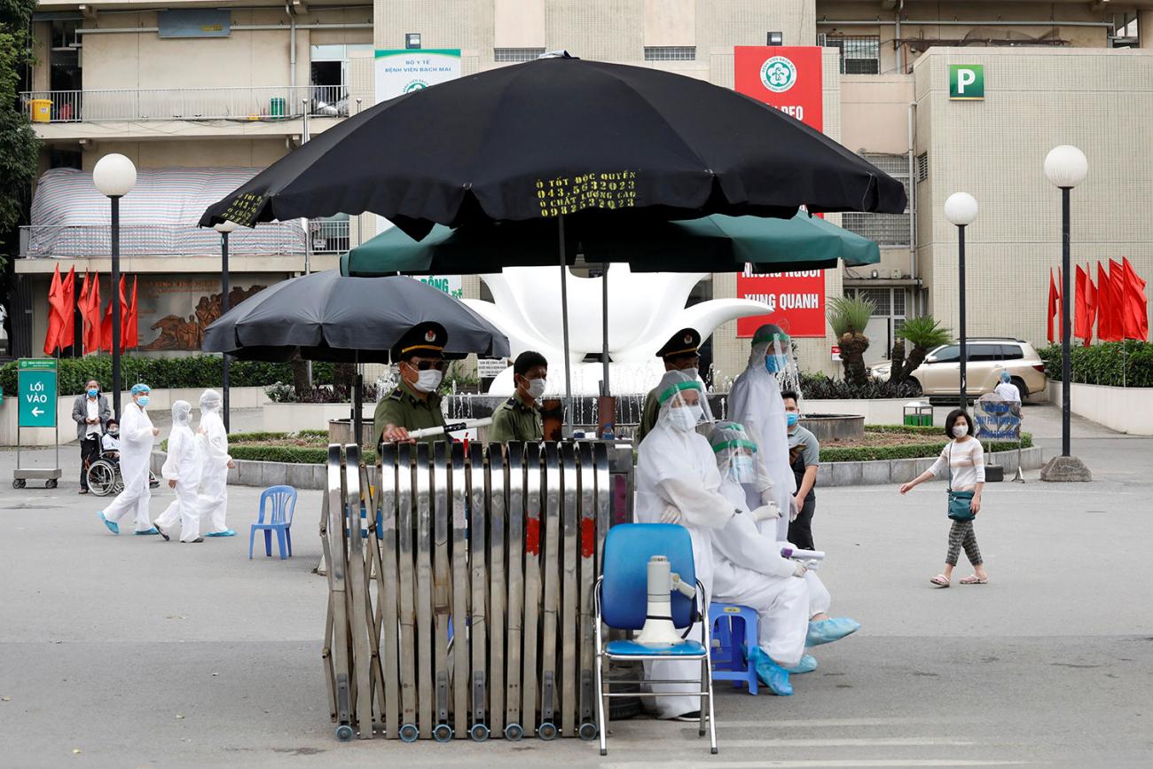 Photo shows the hospital from the outside with a simple triage set up with a black umbrella. 