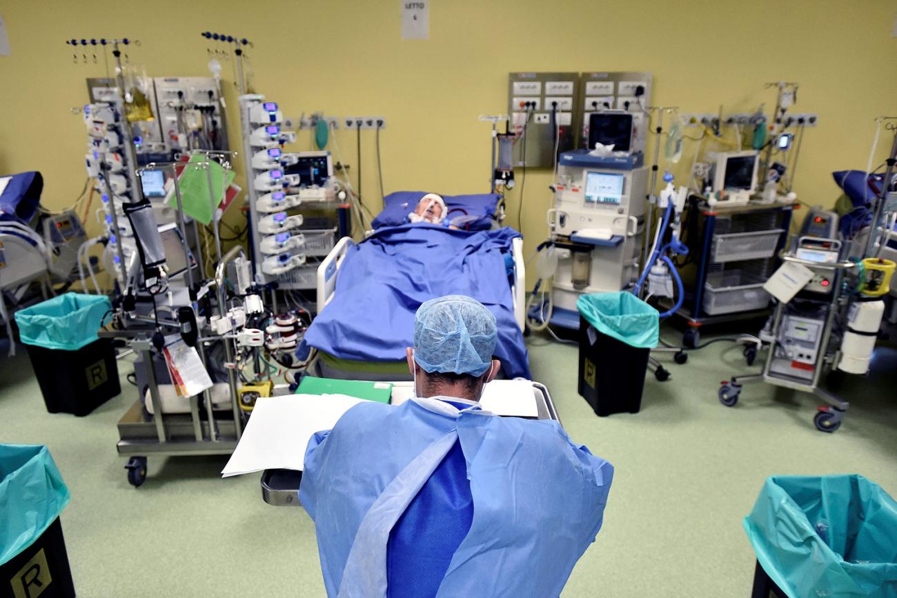 Image shows a health worker from behind in a room where someone suffering from coronavirus lies in a bed surrounded by medical equipment. 