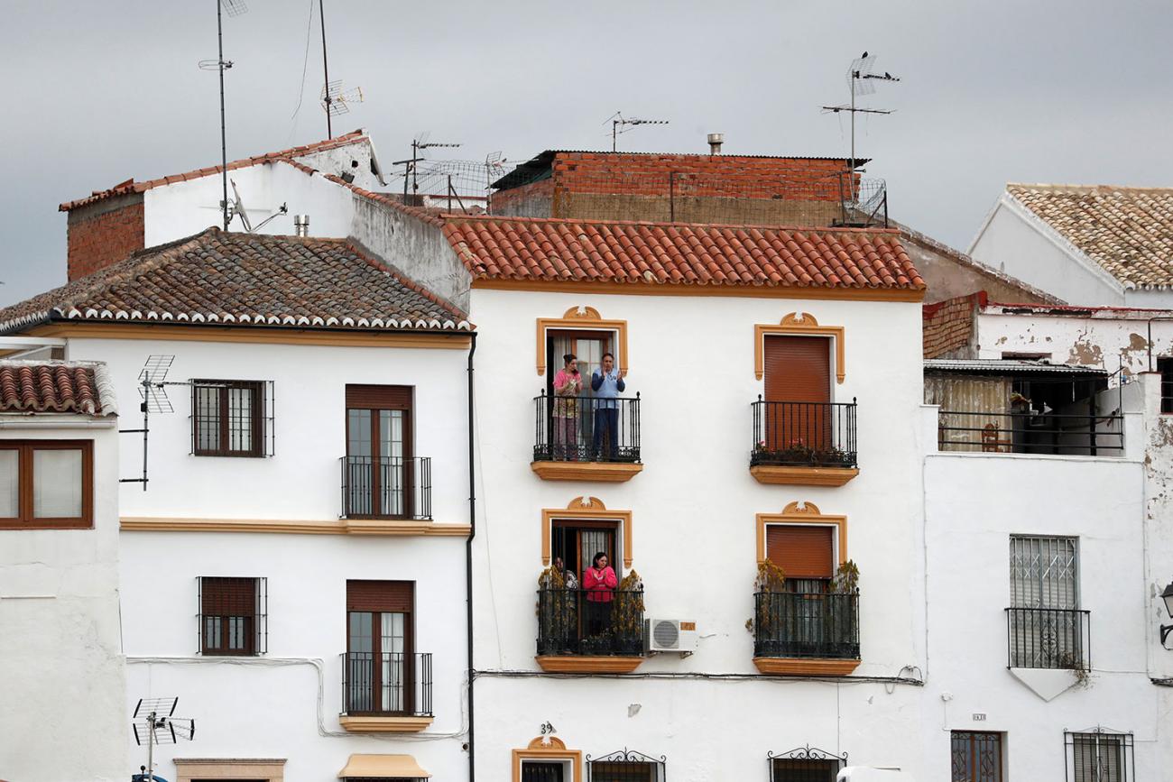 The picture shows a Spanish residential building with people on the balcony cheering. 