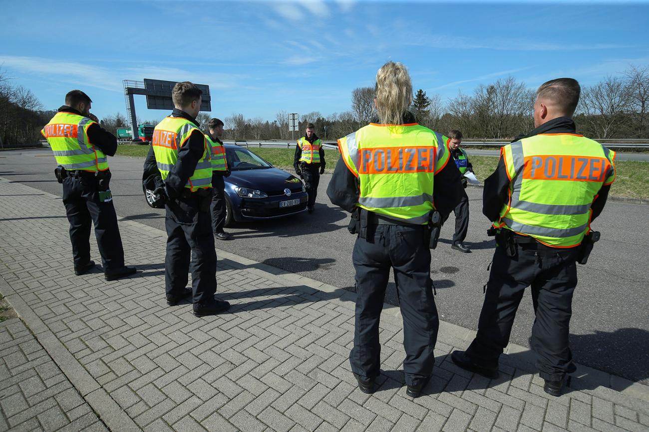 The photo shows several uniformed officers wearing yellow vests halting motorists at a checkpoint. 