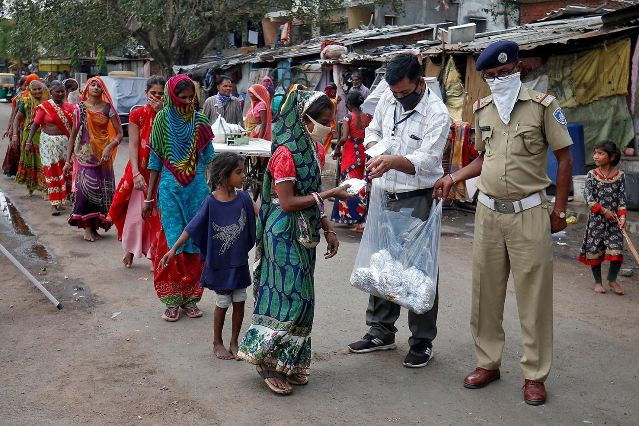 A long line of people, mostly women, stretches off into the distance as two uniformed soldiers wearing masks reach into a plastic bag and pull out foil-wrapped pouches for those in line. 