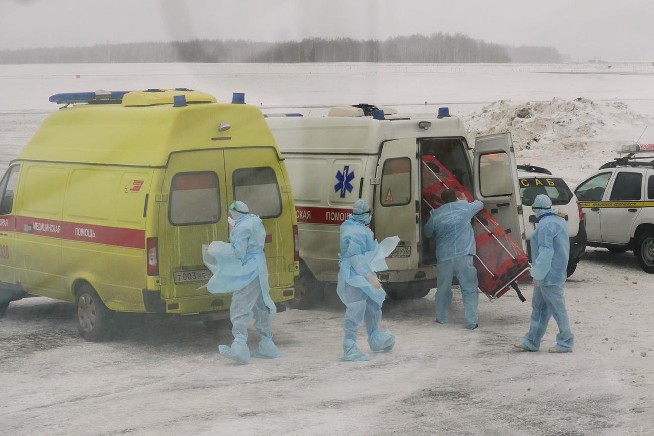 The photo shows several workers in blue protective suits standing outside their ambulances in what appears to be freezing weather. 