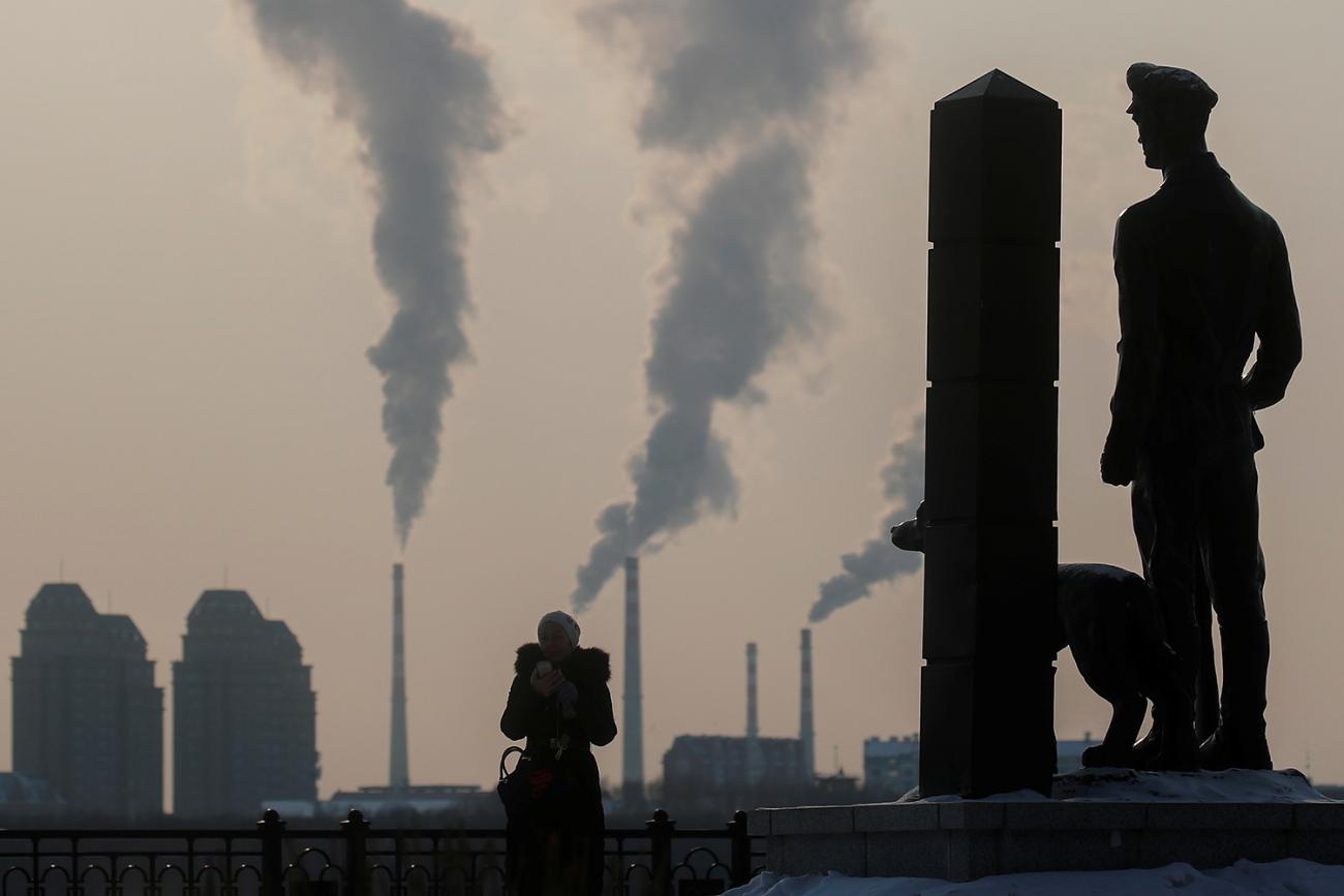 This is a striking photo with the woman, her dog, and the statue all silhouetted against factories belching out smoke across the border. 