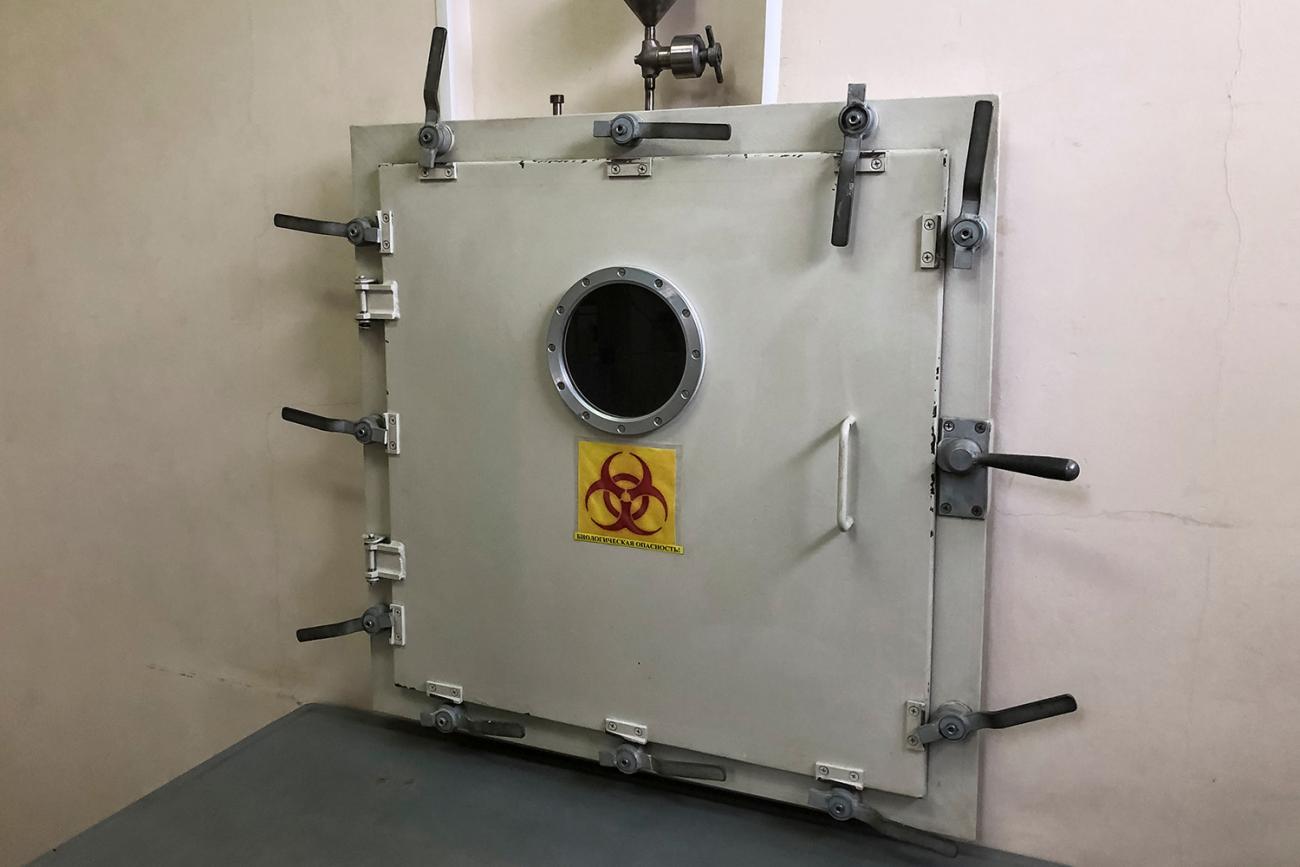The photo shows a beige metal door with all sorts of armored heavy-duty locks and a bright yellow and red hazard sign on the door that reads Biological Hazard. 