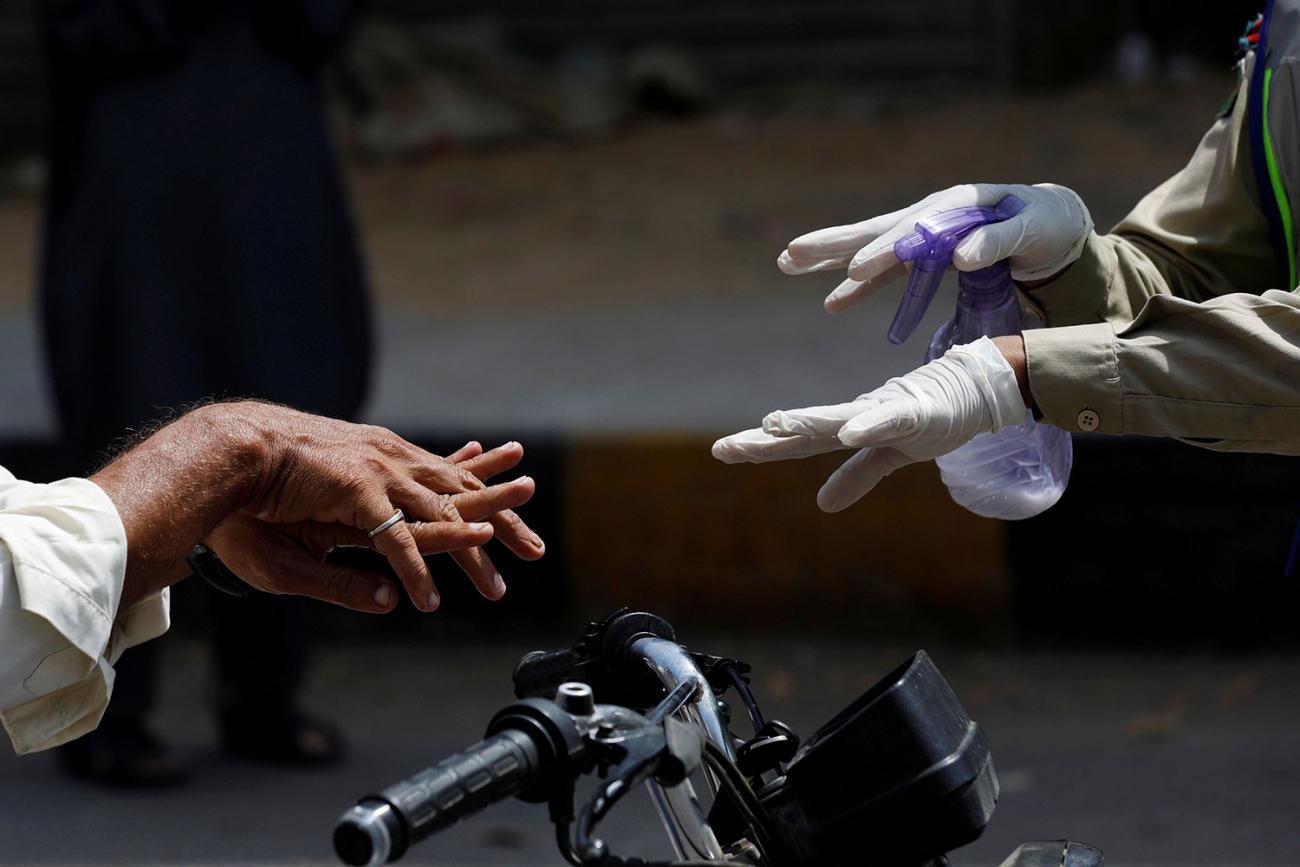 The image shows two sets of hands, one wearing gloves and  demonstrating how to wash between the fingers and the other pair of hands actually doing it. 