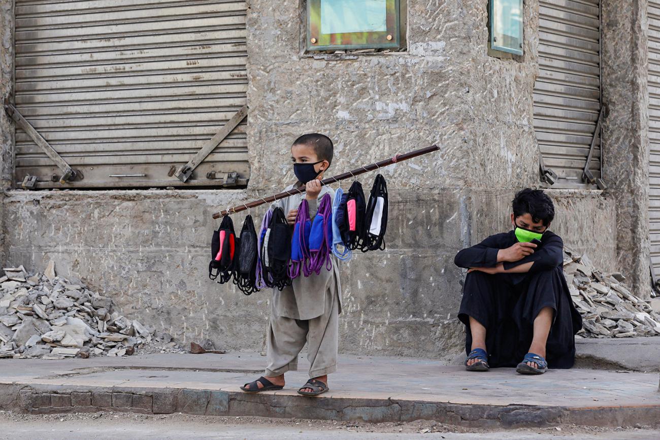 Photo shows the boy wearing a mask with several more tied around a stick as he advertises his wares. 