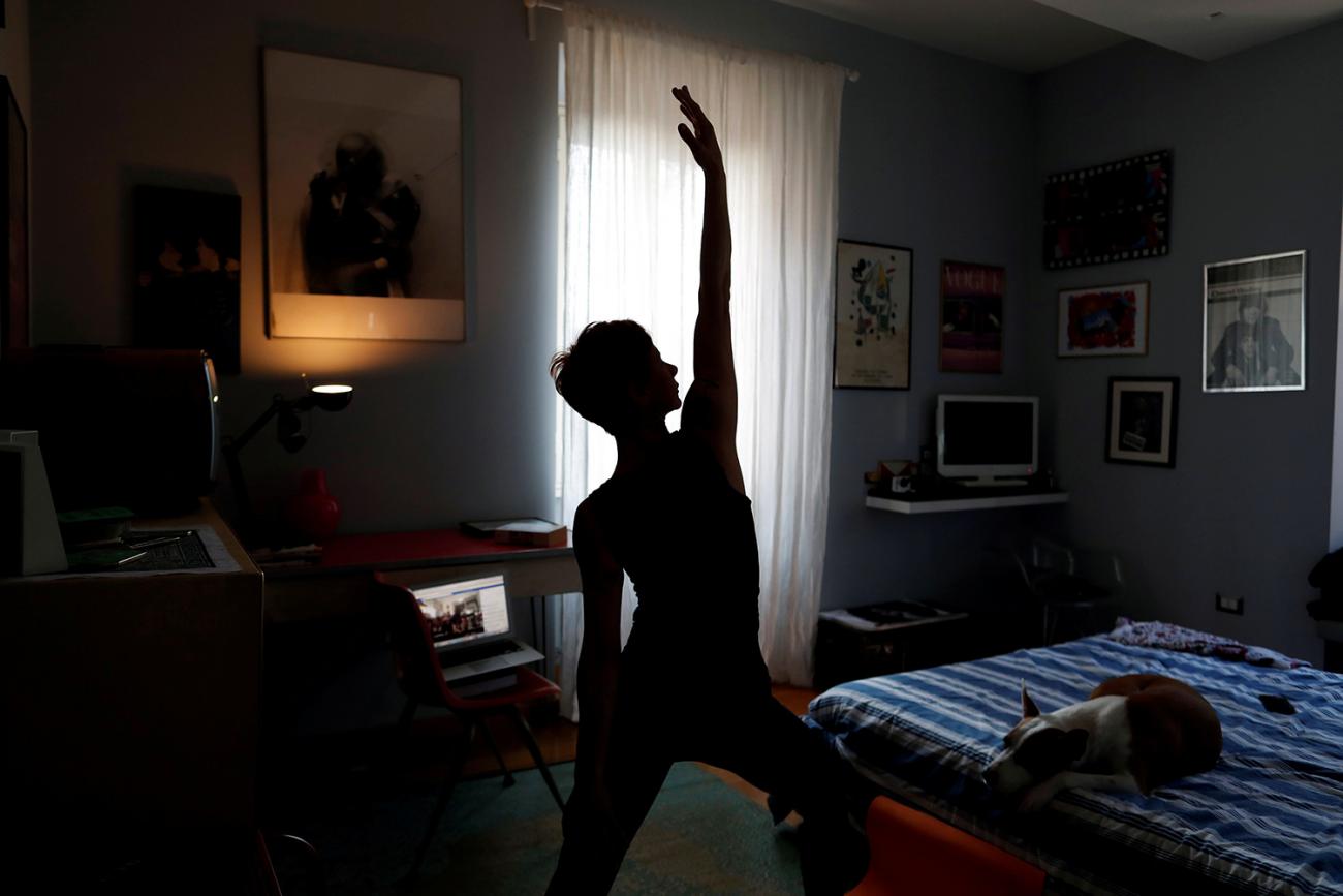 The photo shows a woman in a pose with one arm held up in the air in a small, dark bedroom. 
