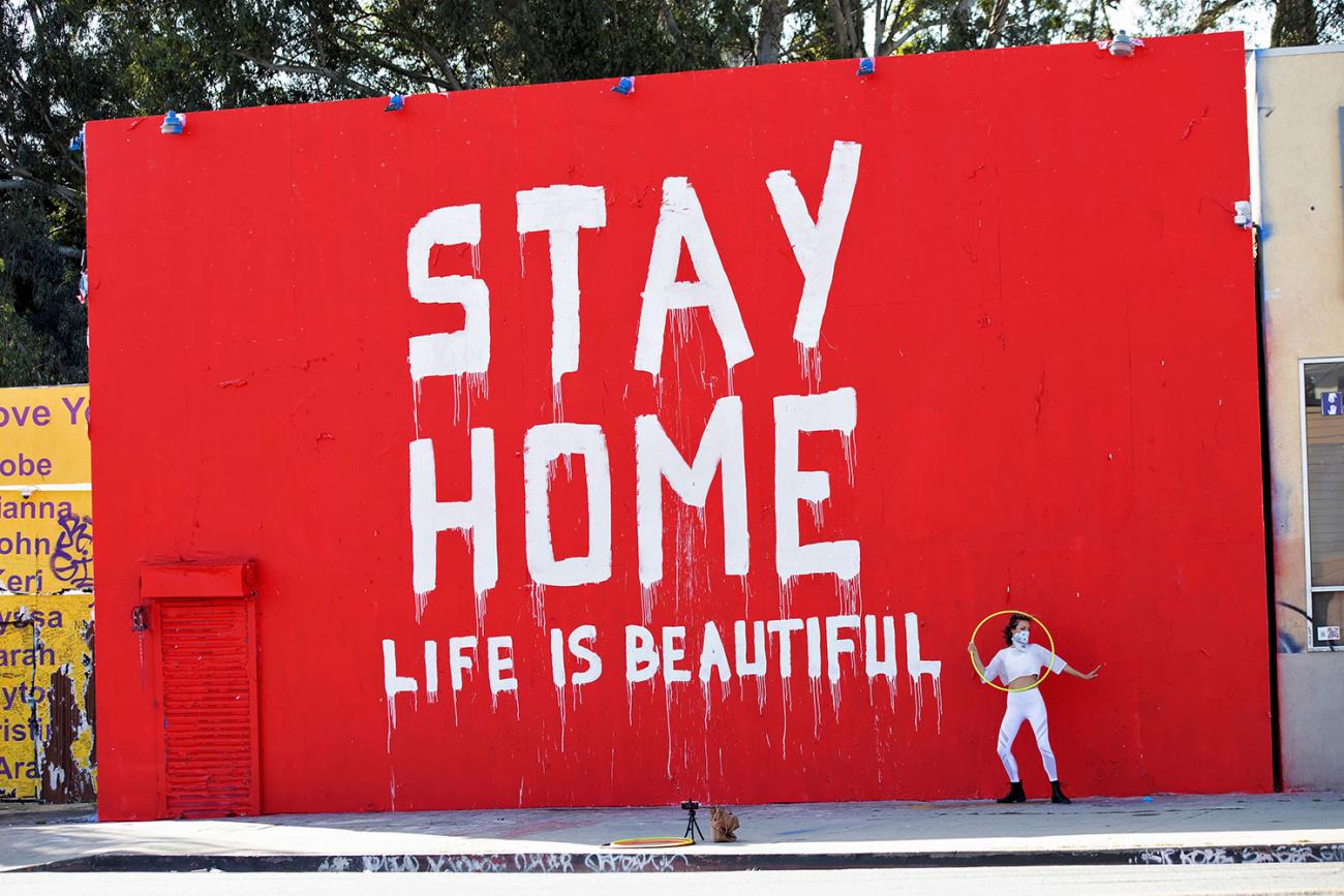 The photo shows a huge striking but crudely hand painted sign that reads "Stay Home / Life is Beautiful." 
