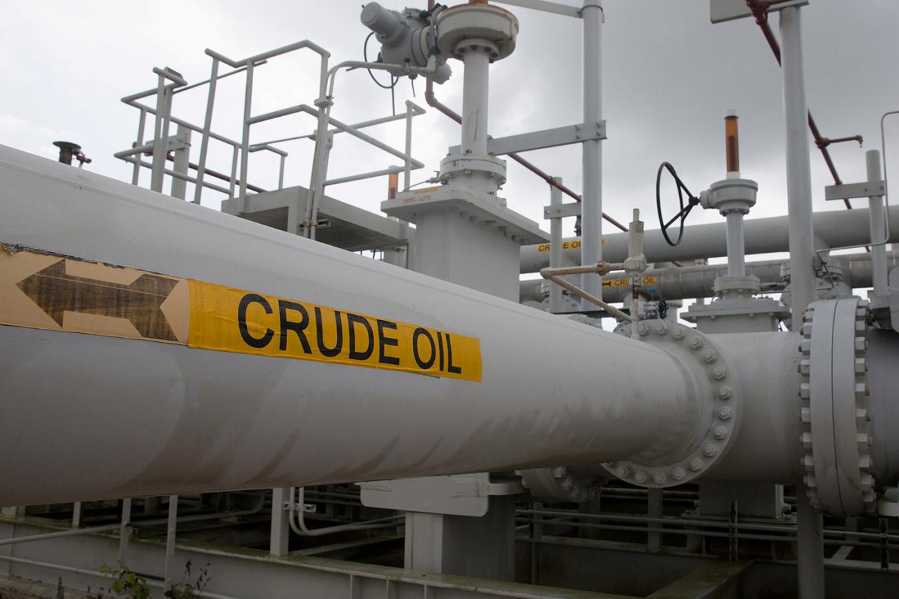 The photo shows an industrial site with machinery for moving oil and a sign with an arrow labeled crude oil, presumably showing the direction of flow.