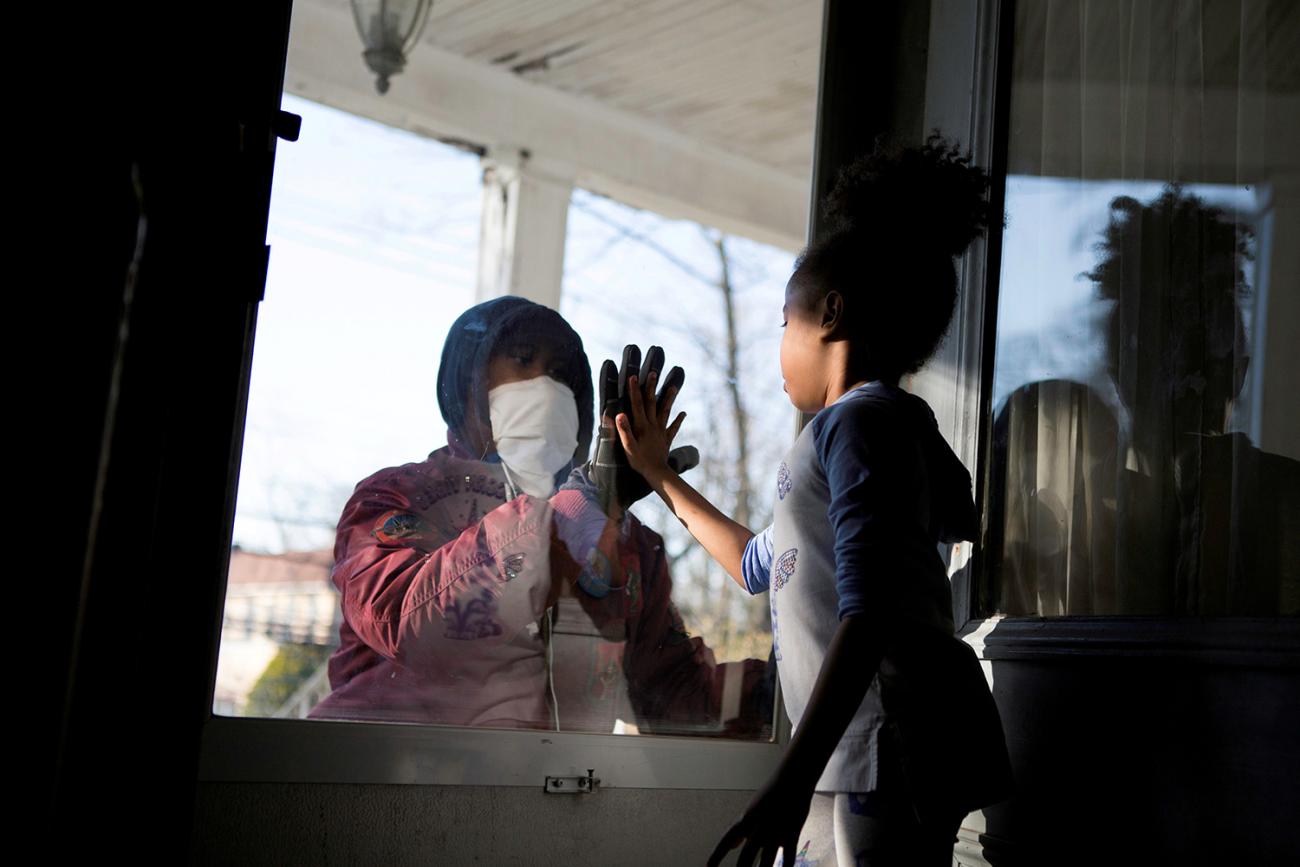 Picture shows the father on one side of the glass holding his hand up, and his daughter places her hand on the glass in response.