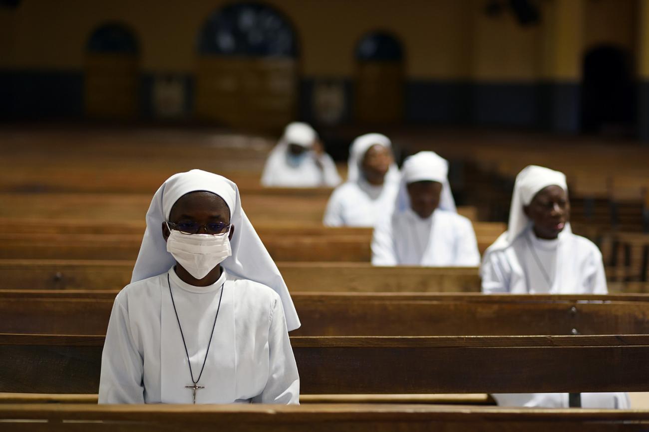 Picture shows a nearly empty cathedral with several nuns sitting in socially distant spacing the nun in the foreground wears a mask. 