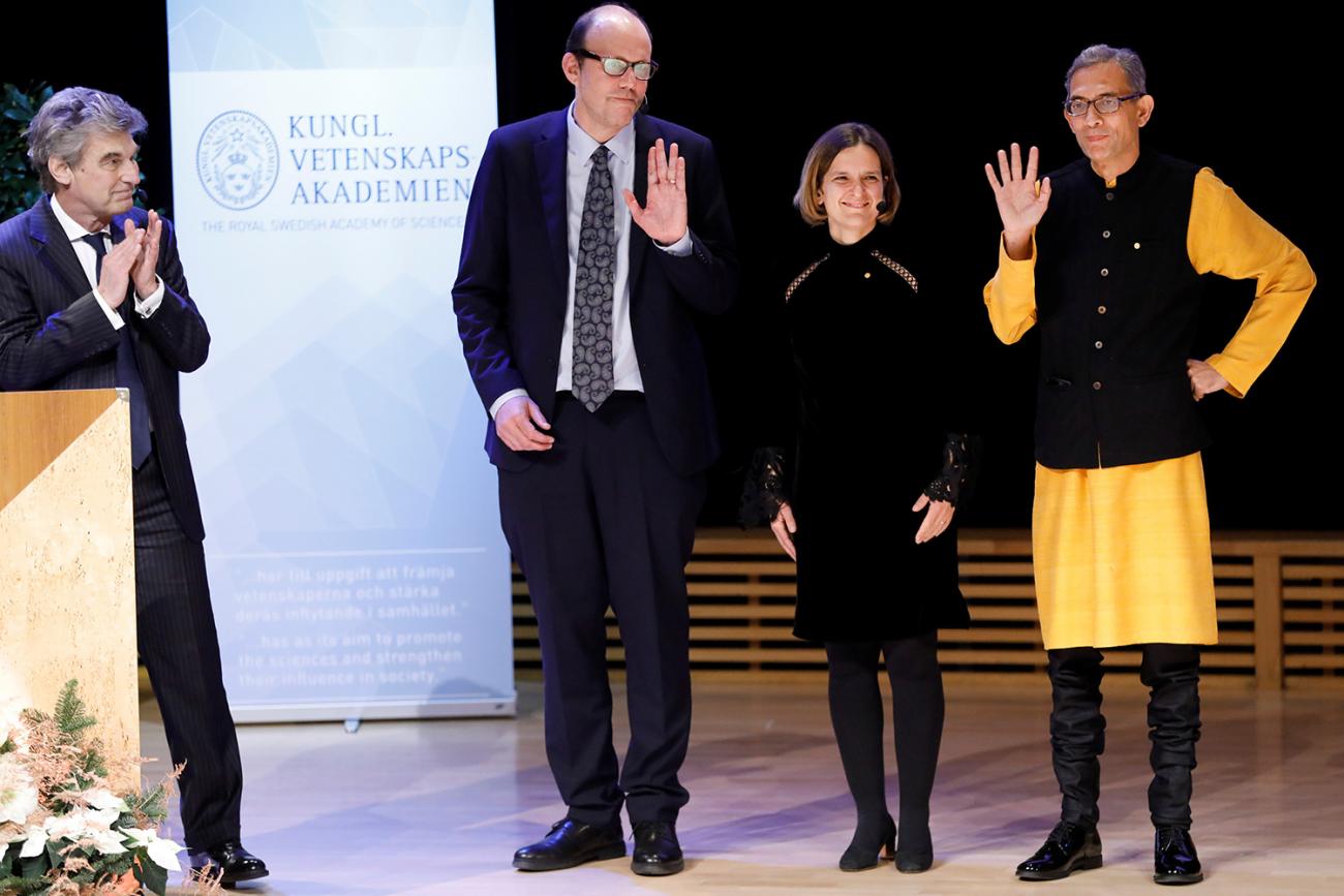Image shows the three nobel laureates posting for pictures on the stage and waving at an audience, presumably to thundrous applause. 
