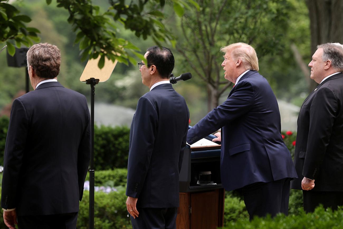 The photo shows the president with Treasury Secretary Steven Mnuchin and Secretary of State Mike Pompeo. He is at the podium speaking. 