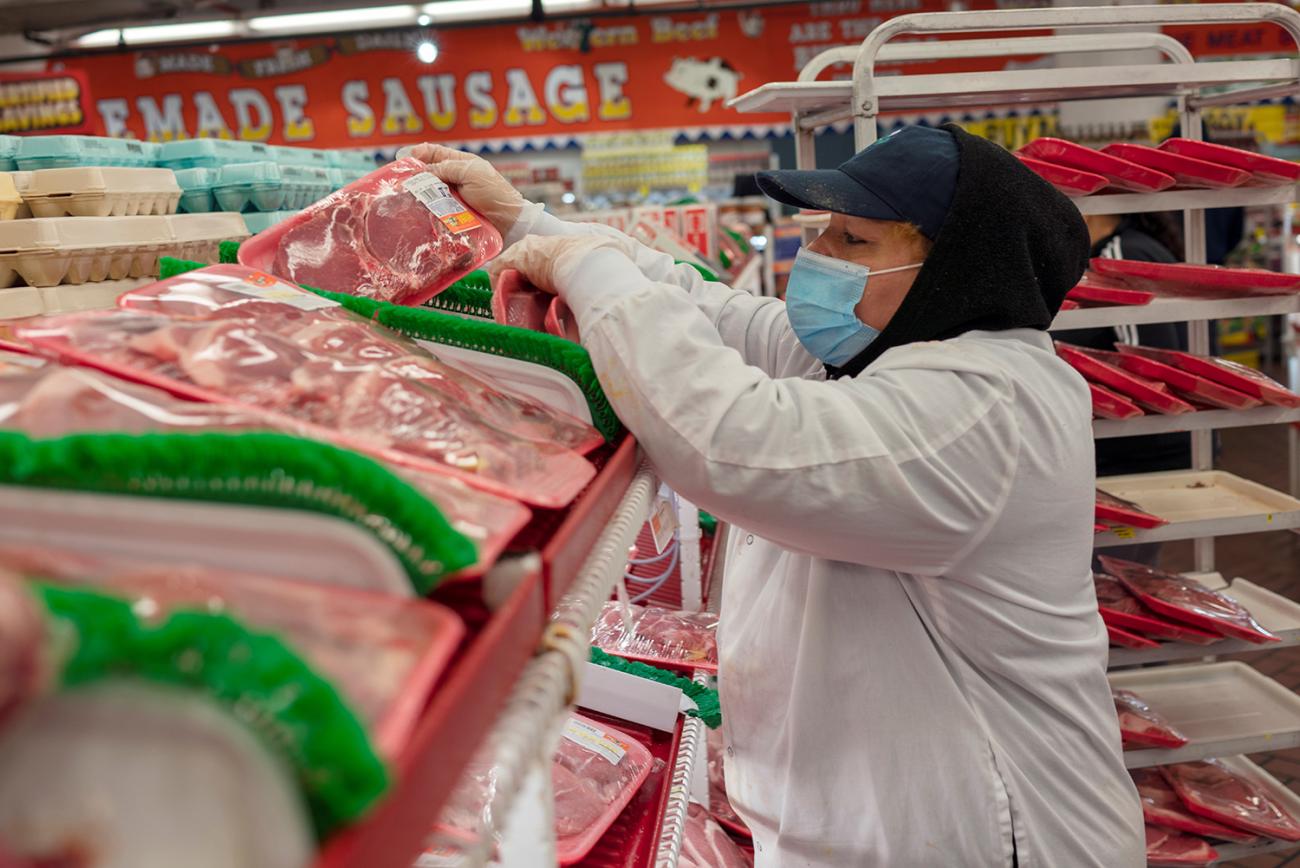 The photo shows a worker filling a meat counter with fresh red meat. 