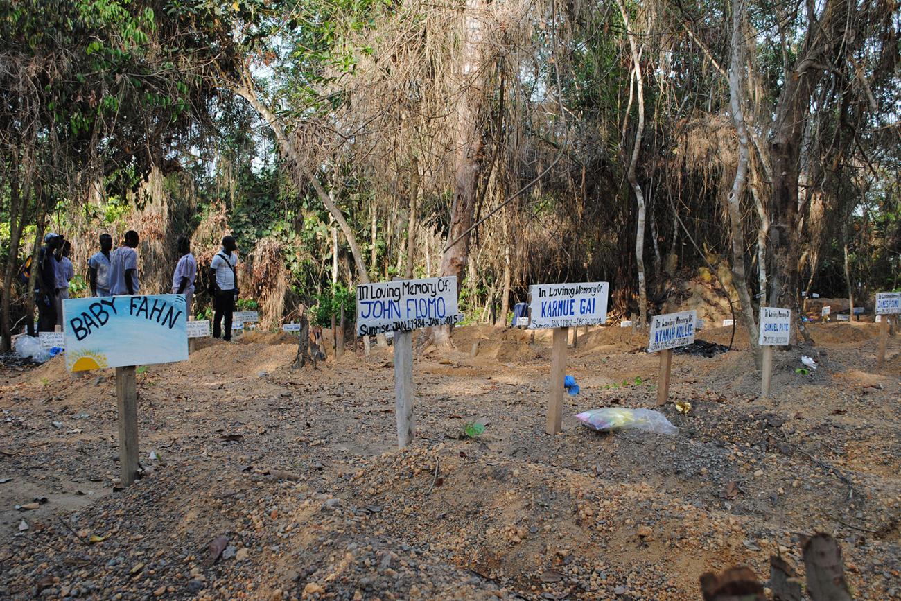The graveyard has what appear to be freshly dug graves adorned with hand-painted wooden markers with names like "John Flomo" And "Baby Fahn."