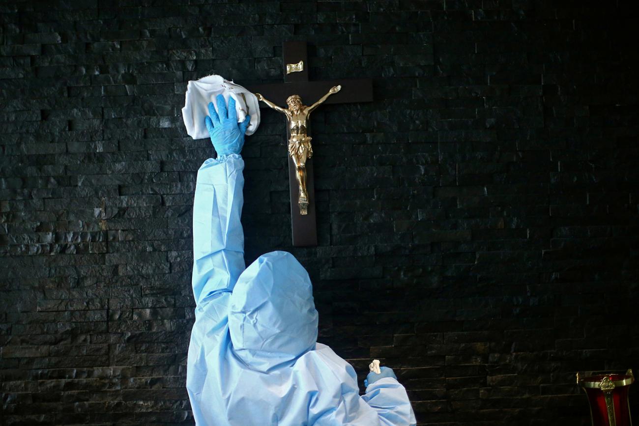 Picture shows a worker in a blue suit reaching up and wiping off a cross. 