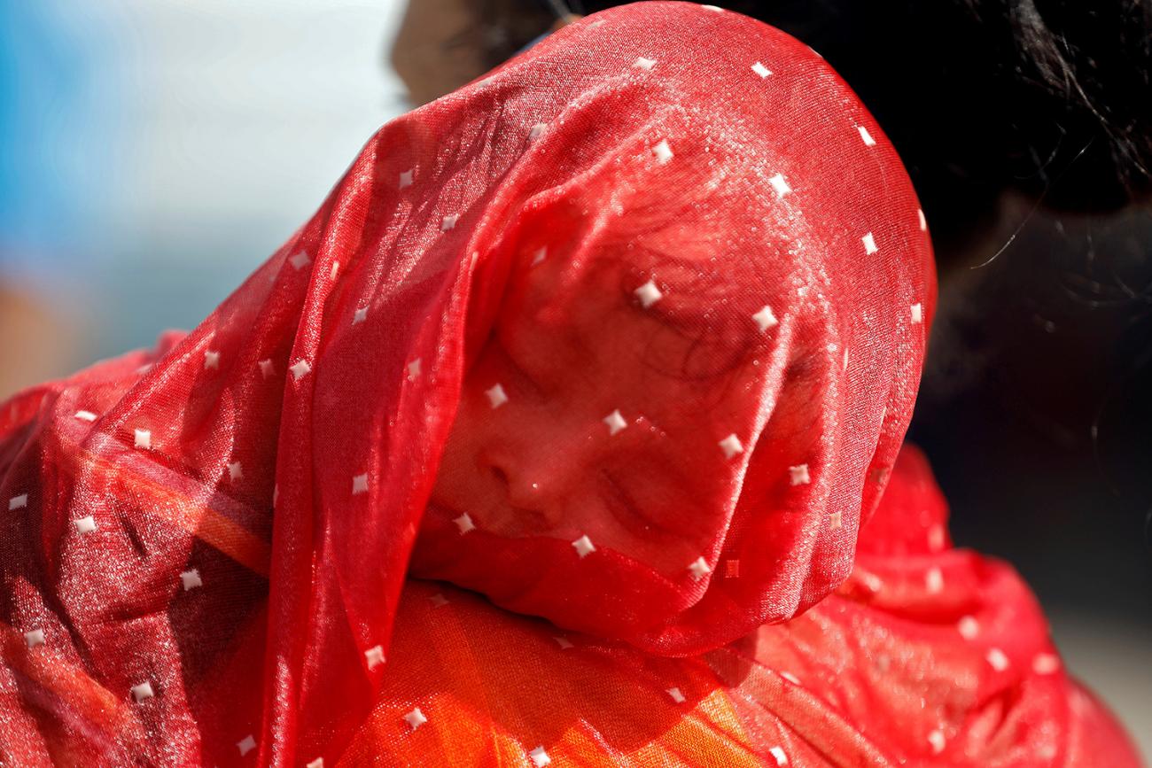 The photo shows the thinly veiled boy wrapped in a red sari resting on his mother's shoulder. 