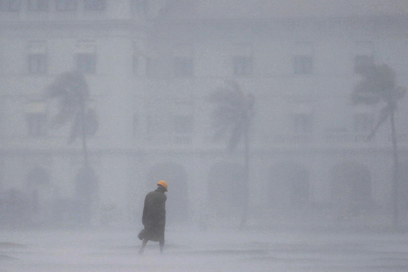 The picture shows a man from a distance walking down the street in a deluge of rainfall. It's raining so hard the man is barely visible in the camera. 