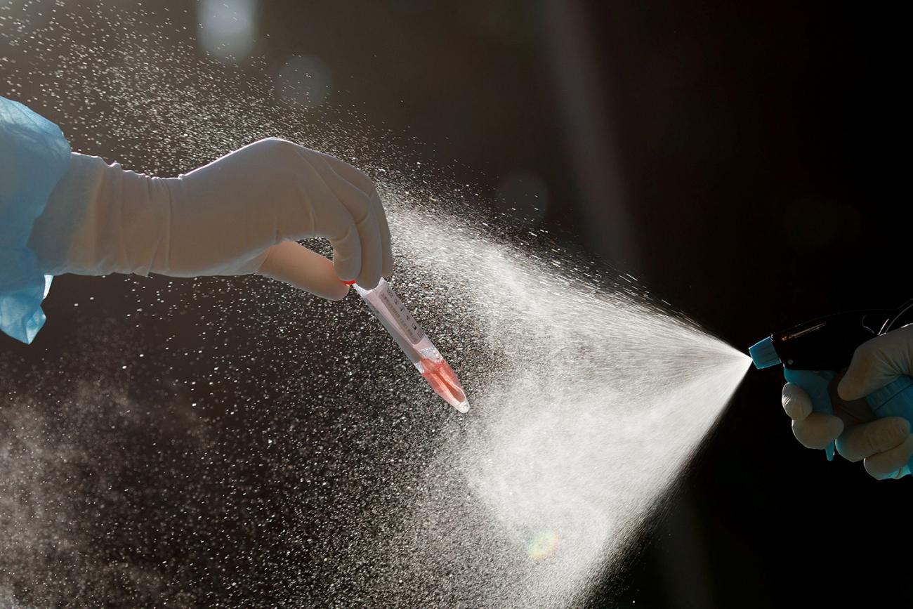 The photo shows one hand holding a small vial with a fluid that appears to be blood while another hand sprays a mist over the whole thing. 