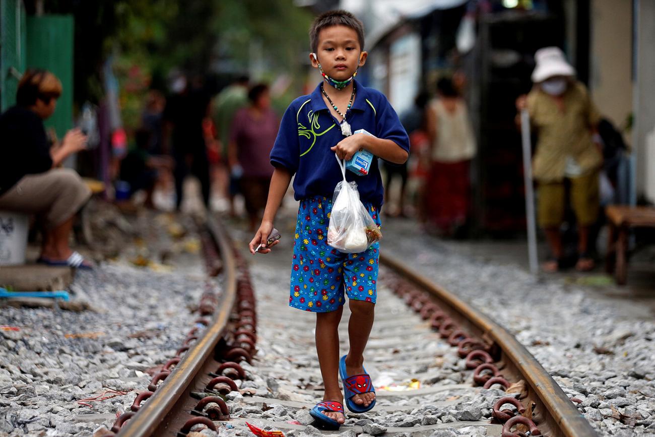 The picture shows a young boy holding a bag of food standing on railroad tracks.