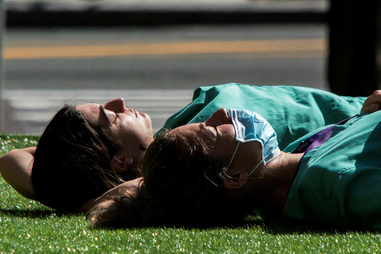 The photo shows two health workers laying on the grass in the warm spring sun.
