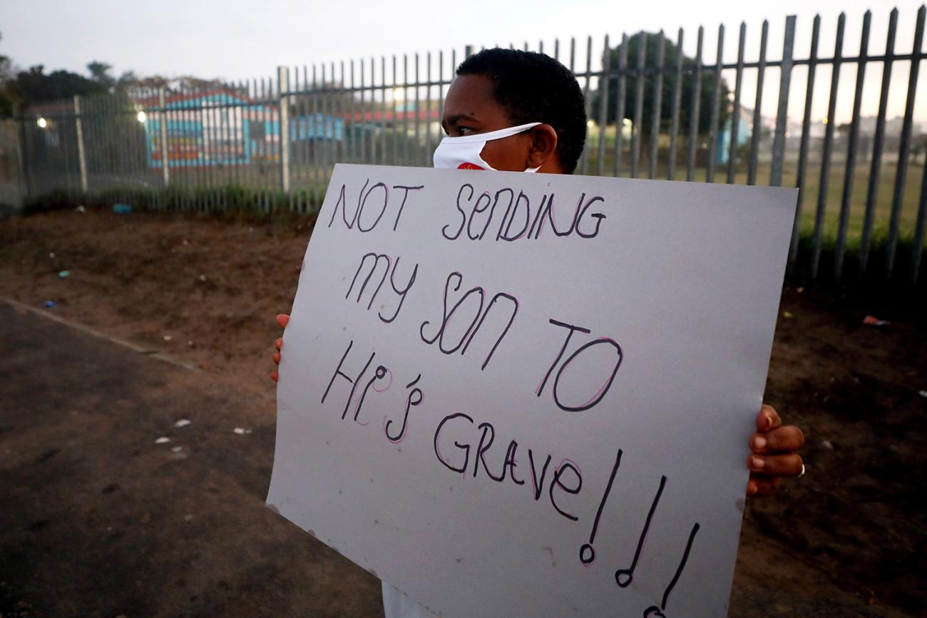 The picture shows a man wearing a facemask holding a sign that reads, "Not Sending My Son to His Grave." 