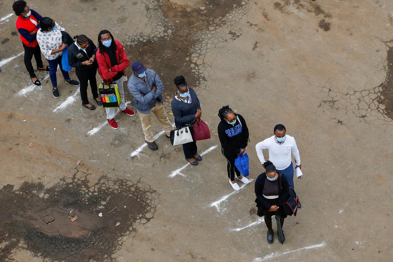 The photo shows several people standing in a line, separating themselves according to lines marked on the ground. 